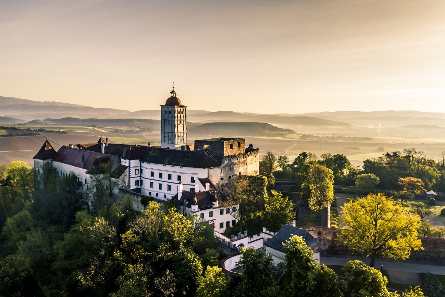 Schallaburg im Sonnenlicht. Vor der Burg grüne Bäume, hinter der Burg hügelige Landschaft