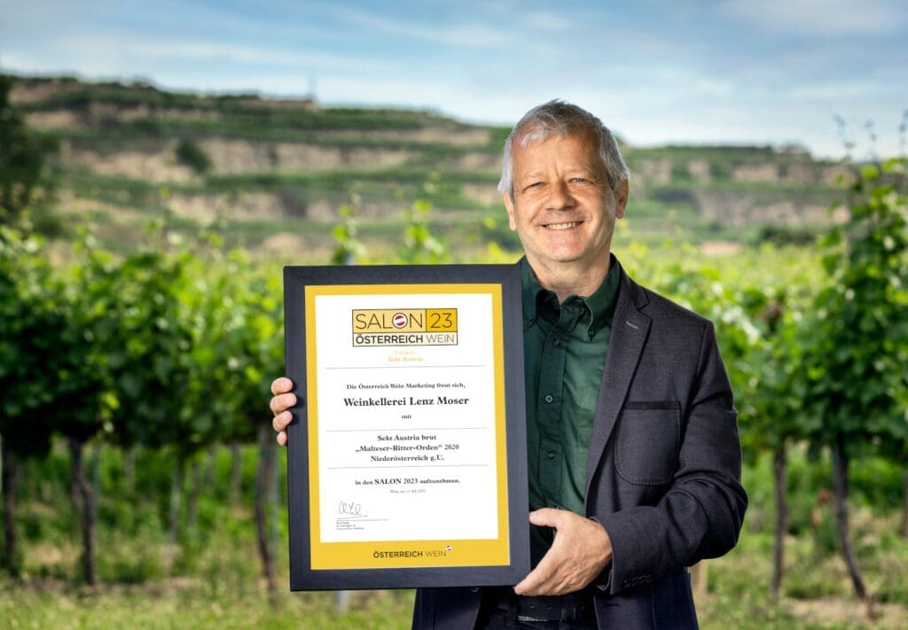Chef Önologe von Lenz Moser mit der Urkunde in der Hand vor einem Weingarten.