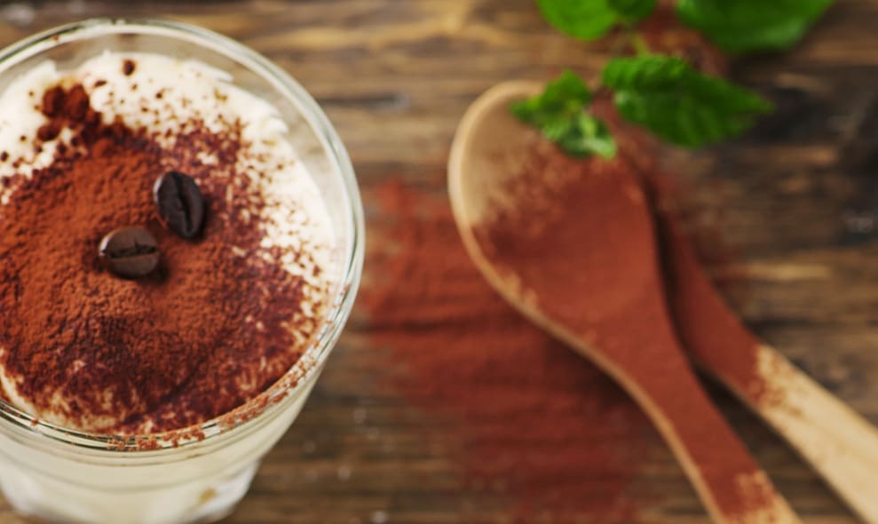 Bieramisu: Tiermaisu in Bier geschichtet mit Minzblatt und Kakaopulver auf Holz neben Holzlöffeln